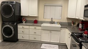 A kitchen with white cabinets, a double washer, a sink, and a stove. - 2 bedroom, 2 bath farmhouse (Blythe)