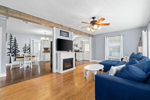 Un salon moderne avec une cheminée, un canapé bleu et un coin repas comprenant une table et des chaises blanches.