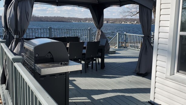 Eine Terrasse im Freien mit Grill, Sitzgelegenheiten und Blick auf einen See.