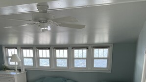 Ein Schlafzimmer mit zwei Betten, einem Deckenventilator, einer Kommode und einem Fenster mit Blick aufs Meer.