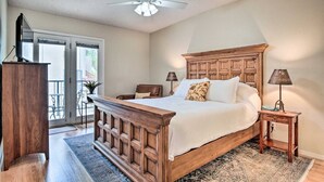 Une chambre avec un lit en bois, un ventilateur de plafond, une table de chevet avec une lampe, et une vue sur l’extérieur grâce à une porte coulissante.