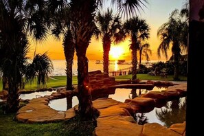 A sunset view with palm trees, a pool, and a pier. - Luxury Waterfront Estate w/ Heated Pools, Private Pier & Walk to Boardwalk! (Kemah)