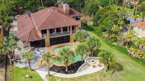 A large house with a swimming pool, surrounded by palm trees and a well-maintained lawn. - Luxury Waterfront Estate w/ Heated Pools, Private Pier & Walk to Boardwalk (Kemah)