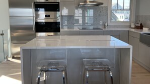 A modern kitchen with stainless steel appliances, a large island with bar stools, and pendant lighting. - Spectacular Views in Center of Town and on the Beach! (Provincetown)