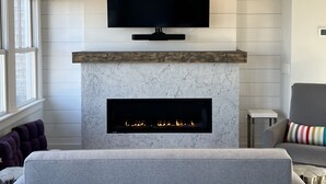 A modern living room with a fireplace, a mounted TV, and a comfortable seating area. - Spectacular Views in Center of Town and on the Beach! (Provincetown)