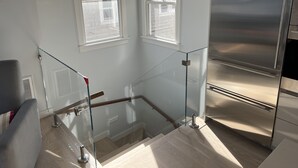 A modern kitchen with stainless steel appliances, a glass staircase, and a view of the outside through windows. - Spectacular Views in Center of Town and on the Beach! (Provincetown)
