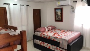 Ein Schlafzimmer mit einem Bett, einem Holzstuhl, einer Tür, einer Klimaanlage und einem Bild an der Wand.