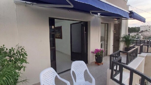 Ein Gebäude mit blauem Markisenbalkon, Glastür und zwei weißen Plastikstühlen davor.