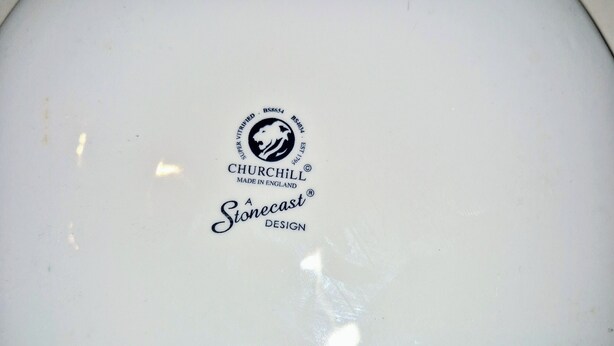 A white ceramic plate with a logo and text indicating it is a Churchill brand, made in England, and designed by Stonecast.