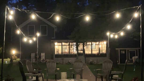 Ein Terrassenbereich im Freien mit Feuerstelle, Stühlen und Lichterketten.