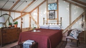 A bedroom with a wooden ceiling, a bed with a red quilt, a wooden dresser, a chair, and a window with a view of trees. - A Family Glamping Adventure Awaits (Victor)