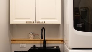 A compact kitchen with white cabinets, a black sink, a countertop with a jar, and a stacked washer and dryer. - A Family Glamping Adventure Awaits (Victor)