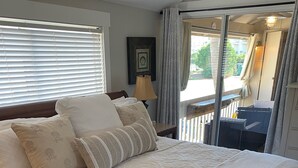 A neatly made bed with a quilt and pillows, a bedside lamp, and a view of the outdoor balcony through a glass door.