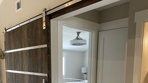 A room with a sliding barn door, a bed with a white headboard, and a ceiling fan.