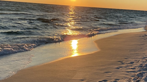A beach with the sun reflecting off the water at sunset.