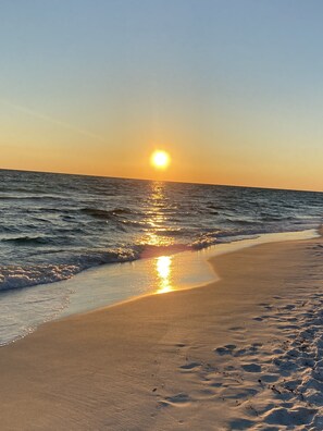 A beach with the sun reflecting off the water at sunset.