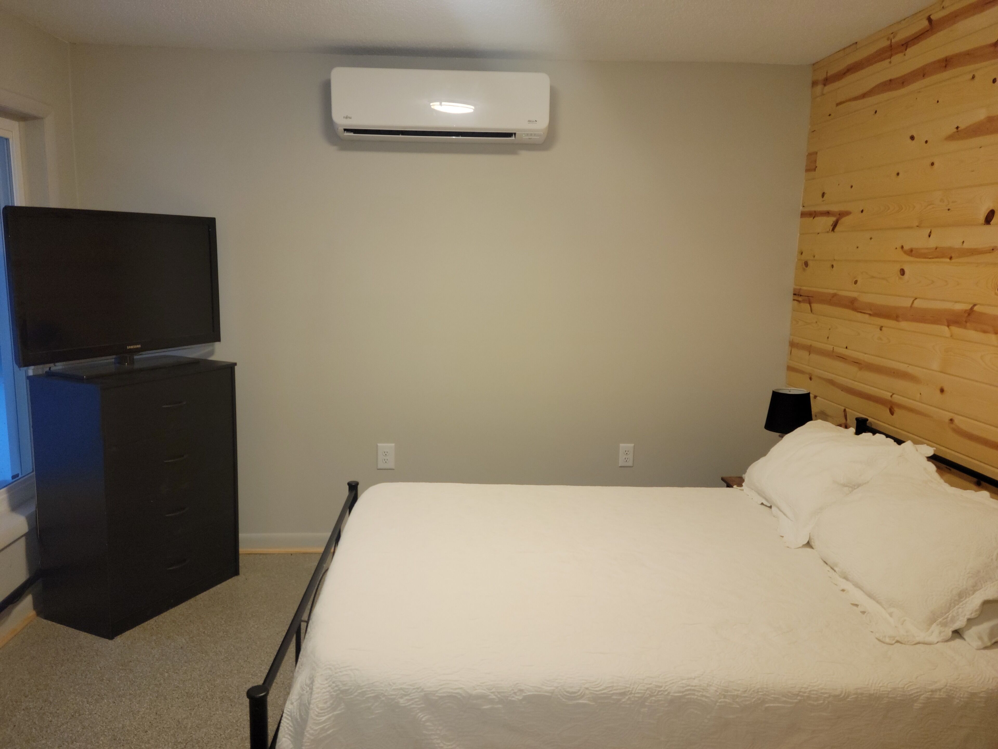 A bedroom with a bed, a dresser, a television, and an air conditioning unit.