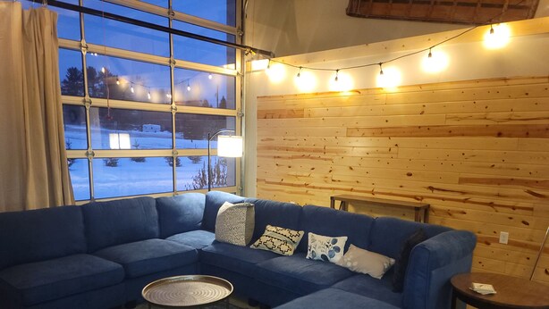 A cozy living room with a blue sectional sofa, a small round table, and a view of a snowy landscape through large windows.