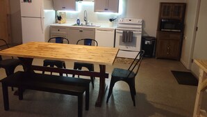 A compact kitchen with white appliances, a wooden dining table, and a bench.