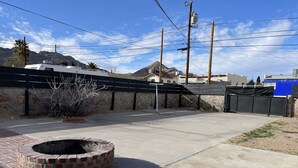 A paved outdoor area with a brick fire pit, a stone wall, and a black fence. - Foothills casita 1 Bedroom (El Paso)