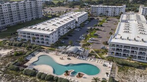 A resort with multiple high-rise buildings, a central swimming pool, and a parking area. - A Wave From it All:  Condo on the Beach (Gulf Shores)