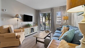 A modern living room with a sofa, armchair, coffee table, and a flat-screen TV. - A Wave From it All:  Condo on the Beach (Gulf Shores)