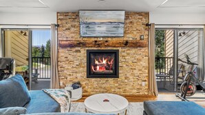 A living room with a fireplace, a sofa, a coffee table, and a bike. - Spacious 3B/3B Condo. Luxury Amenities. ShuffleBoard. HotTubs. 1st FLR. Location (Steamboat Springs)
