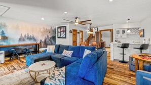 A modern living room with a sectional sofa, a round coffee table, and a mural on the wall. - Spacious 3B/3B Condo. Luxury Amenities. ShuffleBoard. HotTubs. 1st FLR. Location (Steamboat Springs)