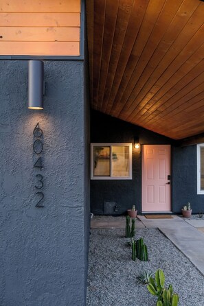 Une maison moderne avec une façade sombre, un plafond en bois et une porte rose.
