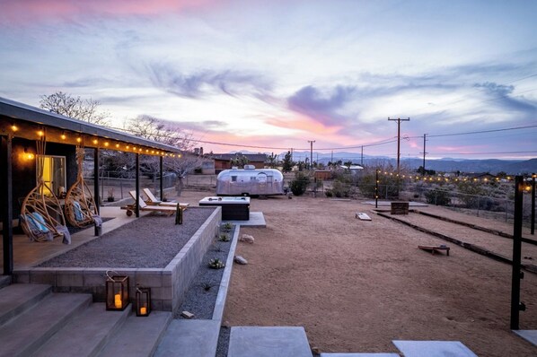 Un espacio moderno para disfrutar del aire libre con un porche cubierto, mobiliario y una caravana al fondo.