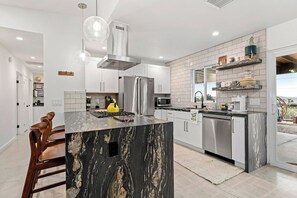 Une cuisine moderne dotée d’un îlot central, d’appareils électroménagers en acier inoxydable et offrant une vue sur l’extérieur.