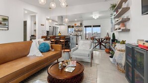 A spacious living room with a brown sofa, a coffee table, and a dining area with a large table and chairs. A kitchen with a bar is visible in the background. - Soul Shine| Amazing Views | Location | Remodeled, Soul Shine| Amazing Views | Location | Remodeled (Joshua Tree)