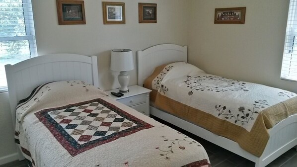 Une chambre avec deux lits, une table de chevet, une lampe et des tableaux encadrés au mur.