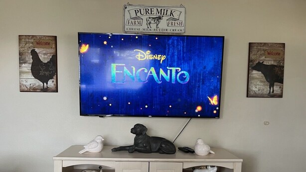 En tv-skärm som visar filmen ”Disney Encanto”, med en skylt med texten ”Ren mjölk” ovanför.