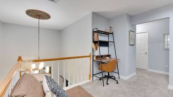 A staircase with a wooden handrail, a cushioned bench with pillows, a black metal desk with a chair, and a decorative ceiling light.
