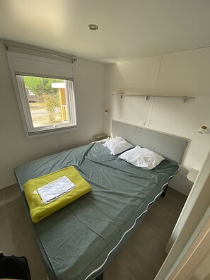 Une petite chambre à coucher, bien rangée, avec un lit simple, une fenêtre et une petite étagère.