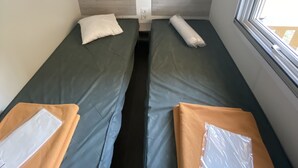 Ein kleines, schlichtes Zimmer mit zwei Einzelbetten und einem Fenster, eingerichtet im funktionalen Stil.