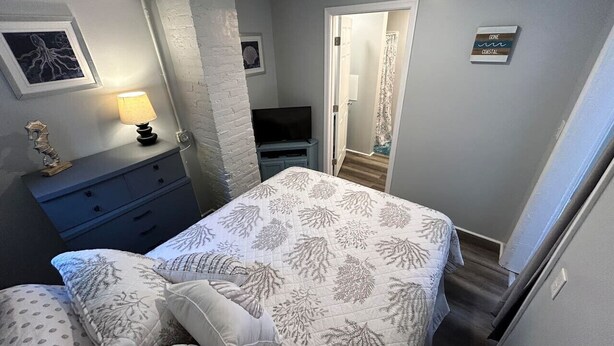 A bedroom with a bed, a dresser, a mirror, and a door leading to another room.