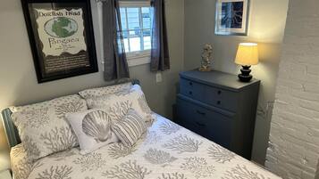 Een slaapkamer met een bed, een dressoir, een lamp, een gecertificeerd diploma aan de muur en een raam met gordijnen.