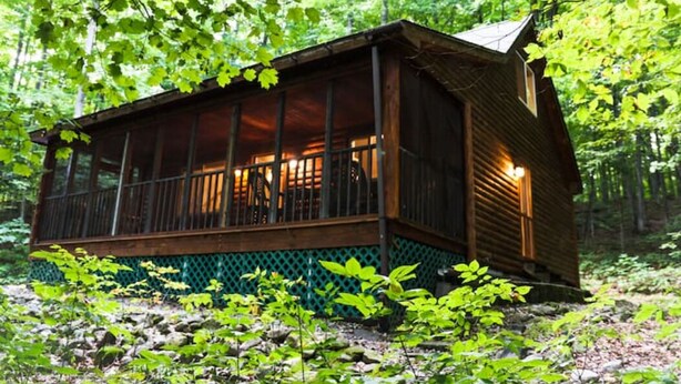 Una cabaña de madera con balcón, rodeada de un bosque frondoso.