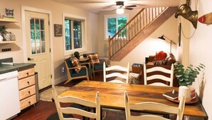 Una cocina acogedora con una mesa de comedor de madera, sillas blancas, una escalera y vistas al exterior.