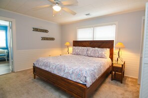 Ein Schlafzimmer mit einem hölzernen Bett, zwei Nachttischlampen, einem Deckenventilator und Wandtafeln mit den Aufschriften 'SEASIDE' und 'SUNBATH'.