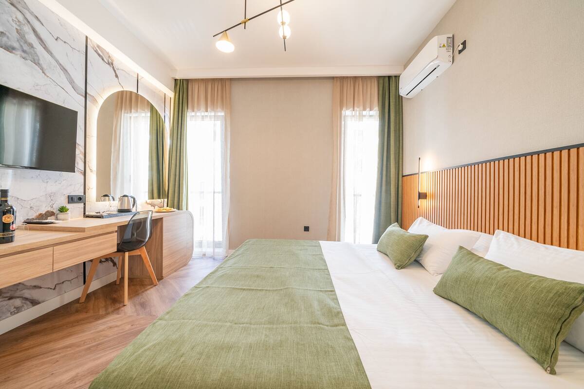 Habitación de hotel con cama, escritorio, silla, televisor y aire acondicionado.