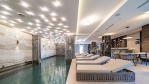 Un área de piscina interior moderna con paredes de mármol y sillones de descanso.