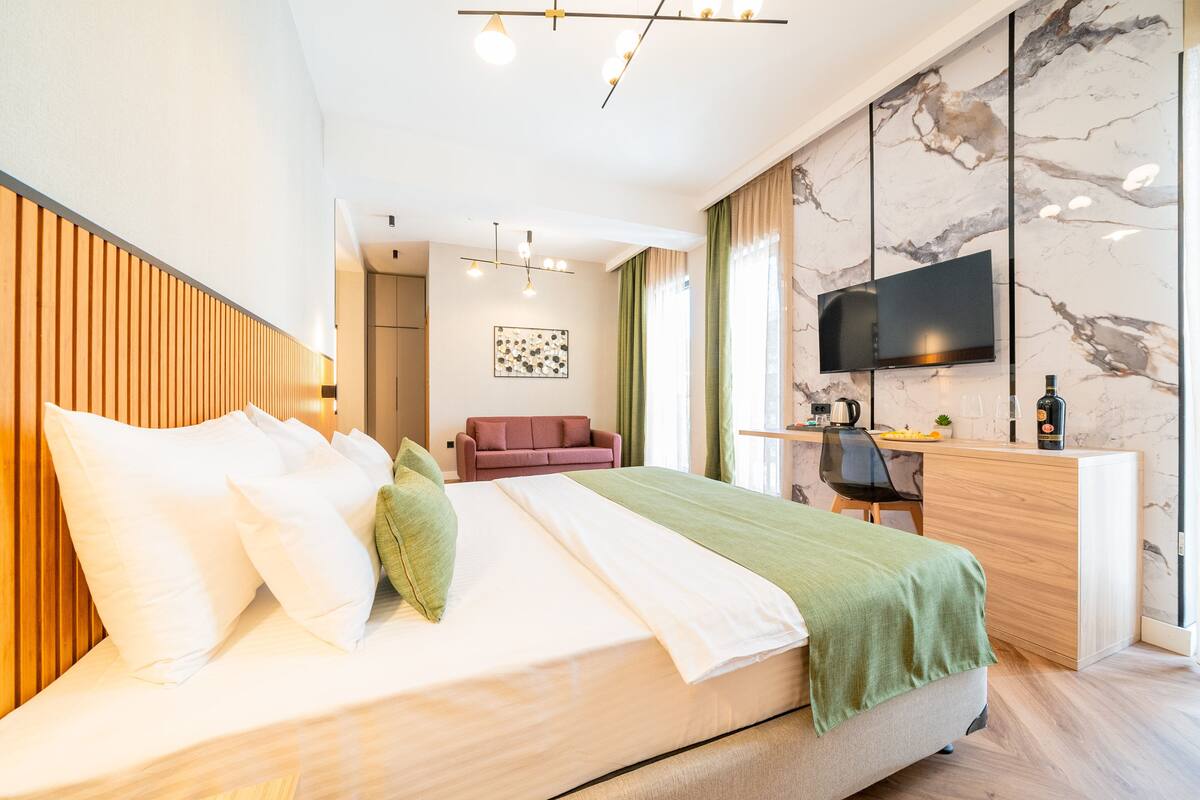 Habitación de hotel moderna con cama, escritorio, televisión y baño al fondo.