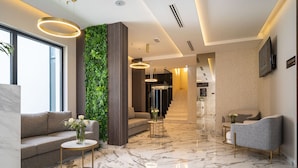 Un vestíbulo moderno con piso de mármol, un jardín vertical verde, un sofá, una mesa redonda de centro y un televisor montado en la pared.