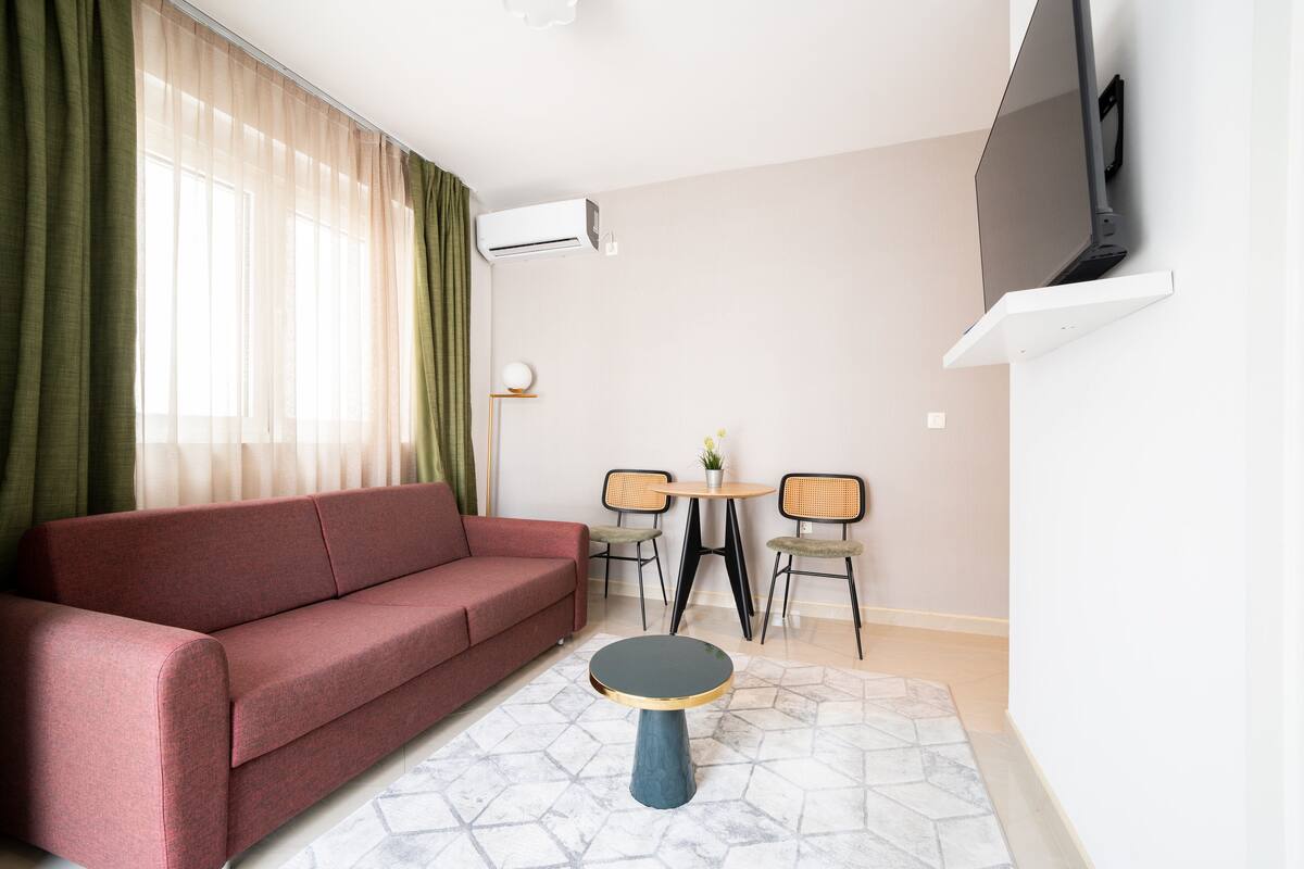 Una sala de estar moderna con un sofá rojo, una mesa redonda con dos sillas y un televisor montado en la pared.