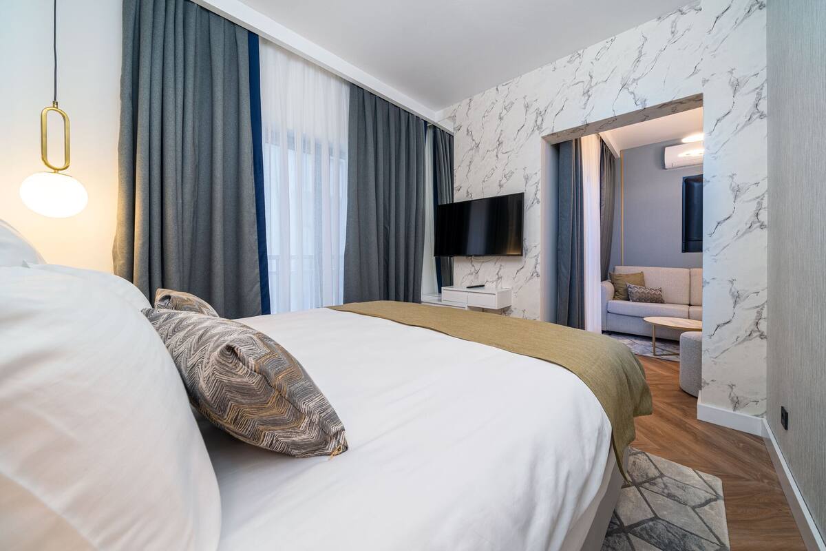 Una habitación de hotel moderna con una cama grande, un televisor de pantalla plana en la pared y un sofá en la zona de estar contigua.