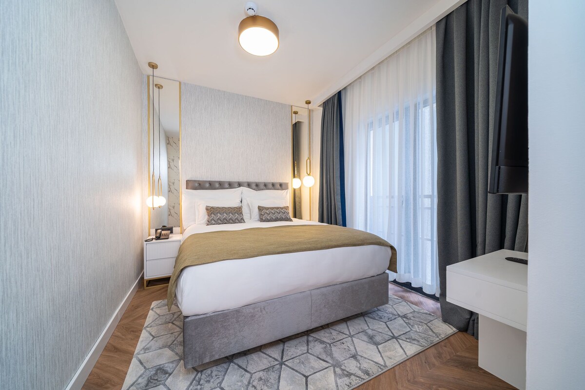 Una habitación de hotel moderna con una cama grande, una mesita de noche, un espejo y un televisor.