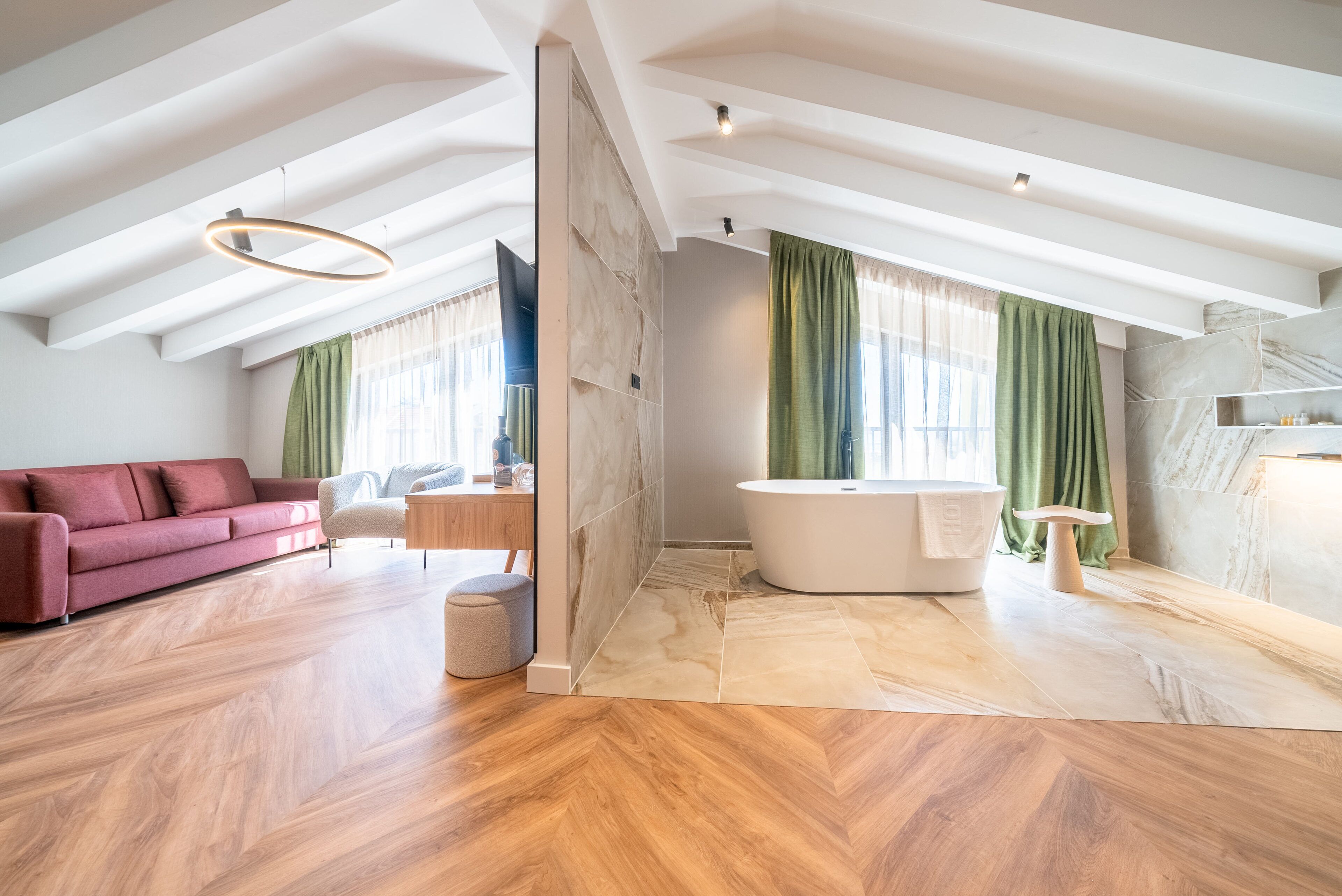 A spacious living area with a large window, a red sofa, a wooden floor, and a modern bathroom with a bathtub.